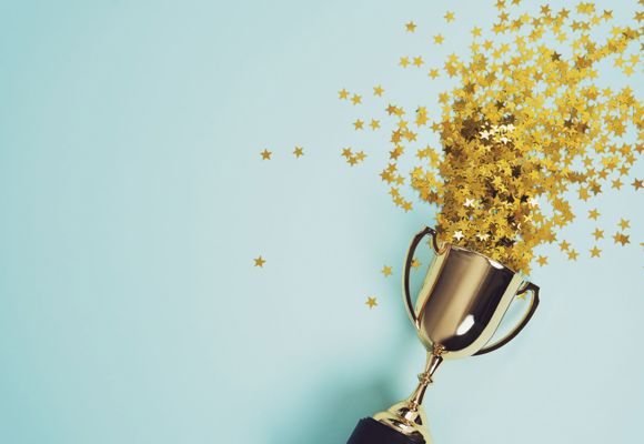 Gold awards cup with gold star confetti flying out.