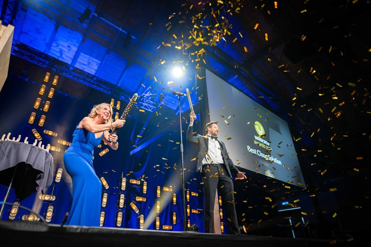 Blonde woman in blue cocktail dress shooting gold confetti into audience.